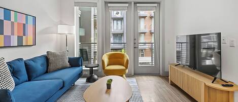 A modern living room with a blue sofa, a yellow armchair, a wooden coffee table, and a TV on a wooden stand.