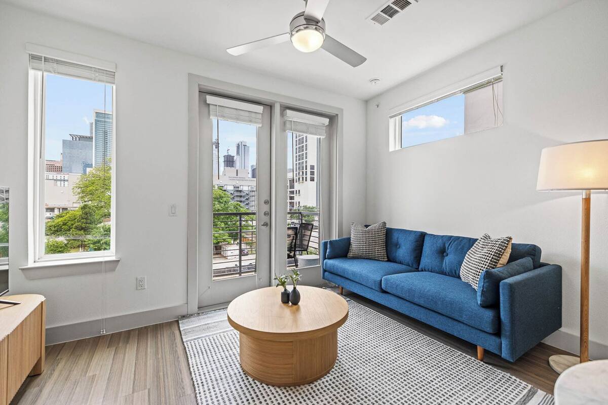 A modern living room with a blue sofa, a round wooden coffee table, and a city view through large windows.