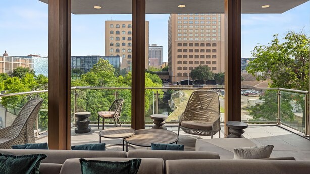 A modern outdoor balcony with wicker furniture, a round table, and a sofa. - Placemakr Austin Downtown, Apartments by Hilton (Austin)