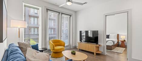 A modern living room with a sofa, armchair, TV, and a ceiling fan.
