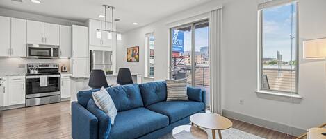 A modern apartment with a kitchen, a blue sofa, and a small round table.