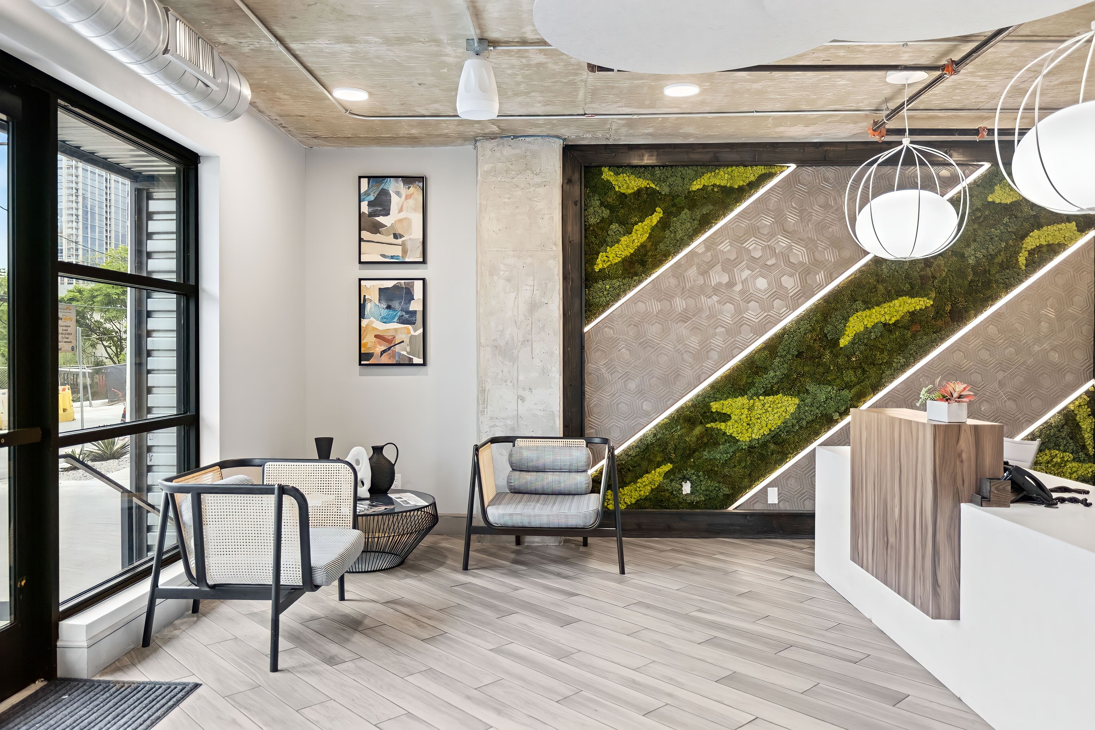 Un espace d’accueil moderne avec un comptoir de réception en bois, deux chaises, une grande fenêtre et un mur vert orné d’un motif géométrique.