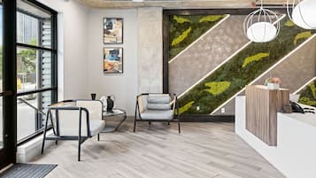 Una moderna zona de recepción con un mostrador de madera, dos sillones, un ventanal grande y una pared verde con un diseño geométrico.