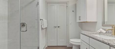 Un baño moderno con cabina de ducha de vidrio, inodoro y muebles de color blanco.