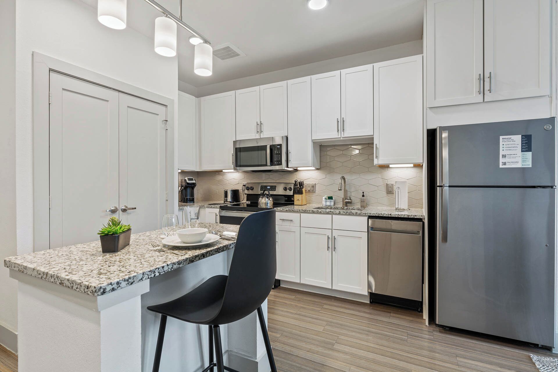 A modern kitchen with white cabinets, a stainless steel refrigerator, a microwave, and a coffee maker.