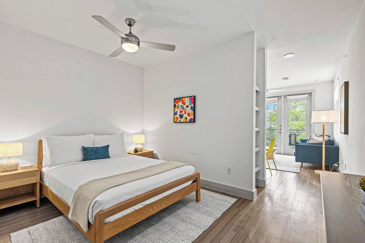 A bedroom with a bed, nightstands, a ceiling fan, a rug, and a painting on the wall.
