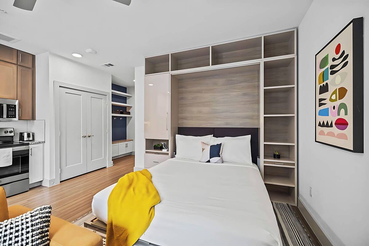 A modern hotel room with a bed, a sofa, a dining area, and a kitchen.