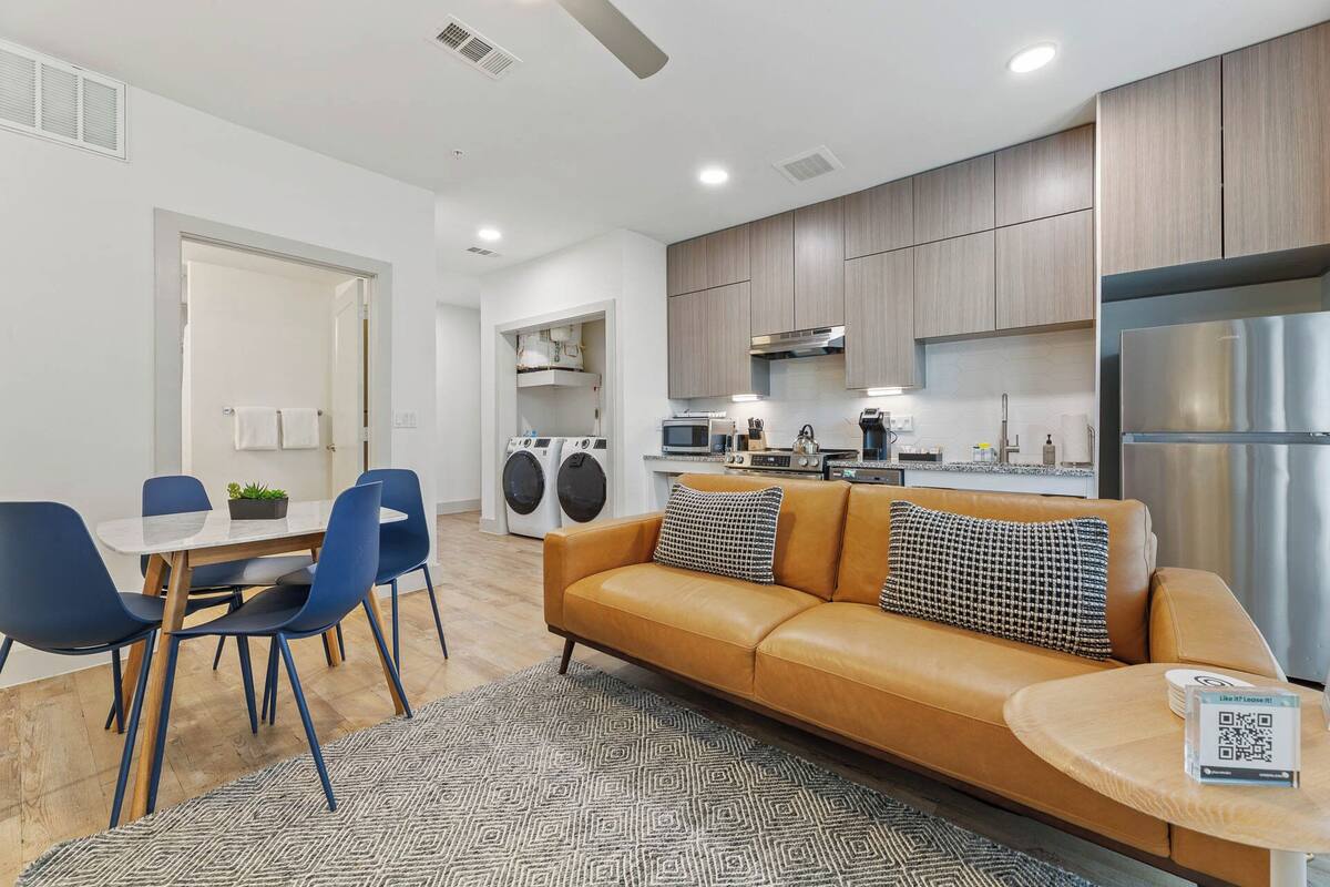 A modern apartment with a dining area, a sofa, a kitchen with appliances, and a laundry area.