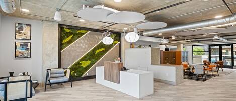 A modern reception area with a white reception desk, seating, and a green wall with a geometric pattern.