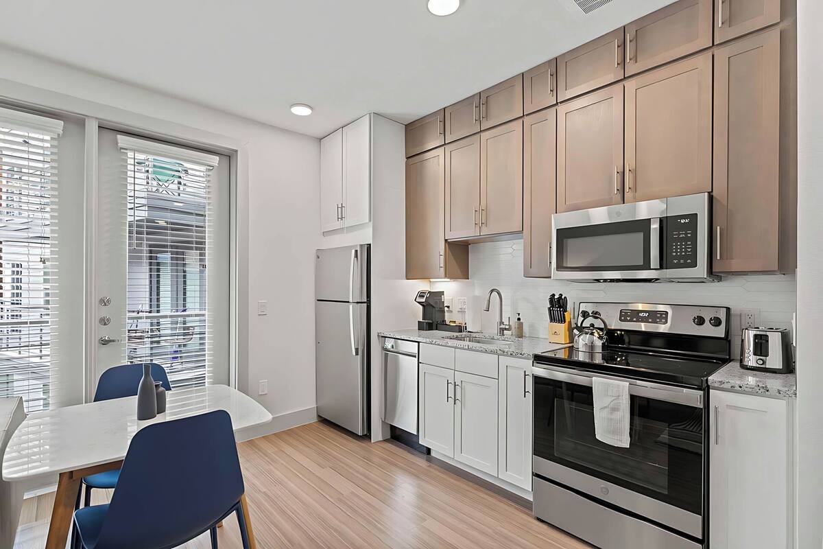 A modern kitchen with white cabinets, stainless steel appliances, and a dining area with a table and chairs.