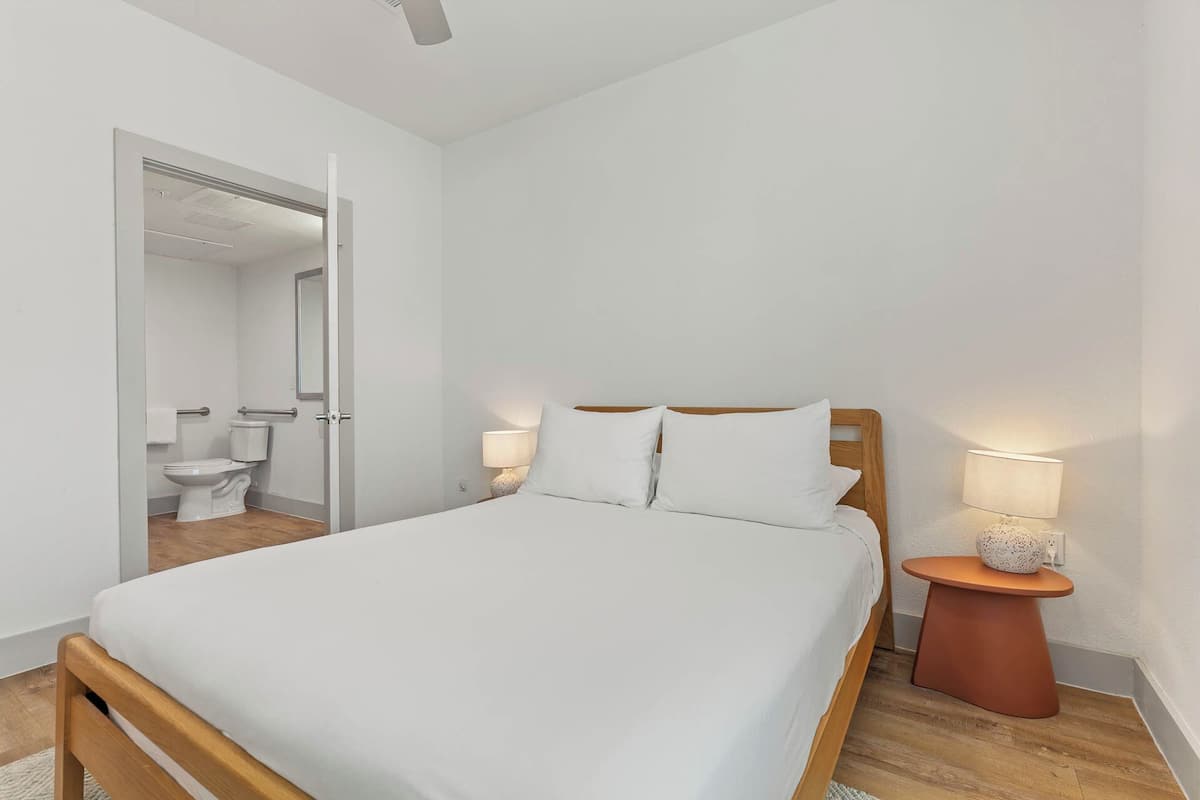 A modern bedroom with a wooden bed, white bedding, and two bedside lamps.