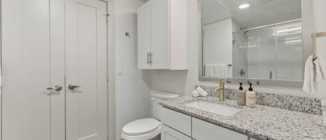 A modern bathroom with white cabinetry, a marble countertop, and a large mirror.