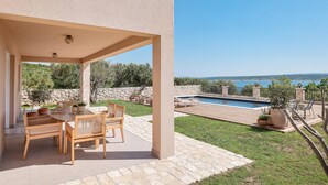 A covered patio with a table and chairs, a swimming pool, and a view of the sea. - Beach front home in Maslenica with sauna (Maslenica)
