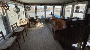 Ein überdachter Außenbereich mit Küche, Holzsitzmöbeln, einer Bar und großen Fenstern mit Blick auf eine Straße.