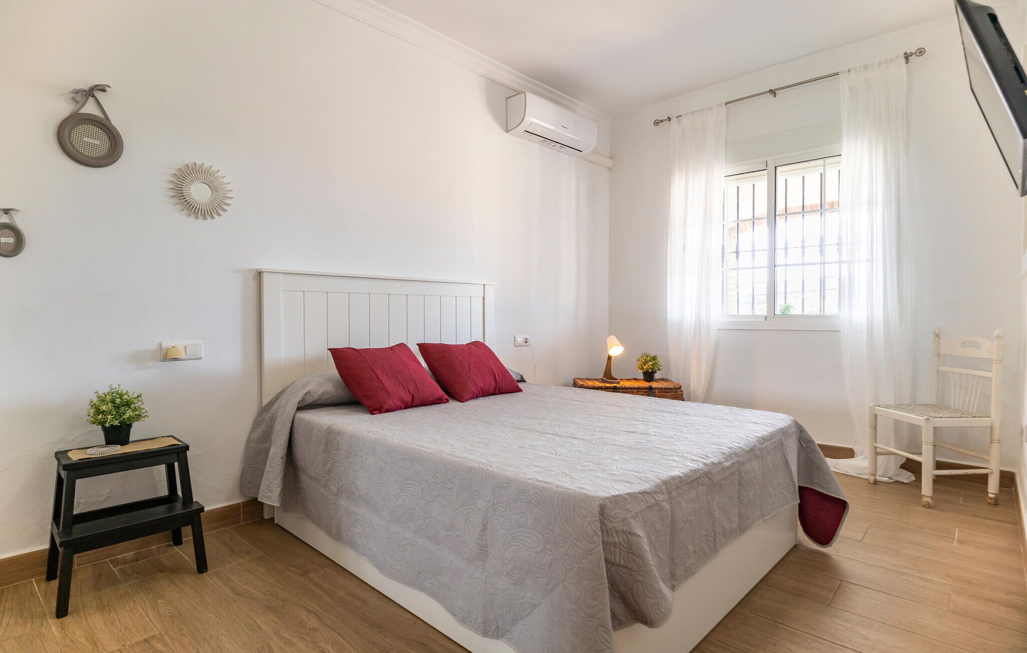 Ein Schlafzimmer mit einem Bett, einem Nachttisch, einem Sessel, einem Fenster mit Vorhängen und einer Klimaanlage.