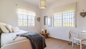Une chambre à coucher avec un lit, deux fenêtres avec des barreaux, une lampe de chevet, une décoration en forme de cœur et une petite chaise.