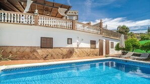 Une piscine bordée de carreaux, un bâtiment blanc doté d’un balcon en bois et un ciel d’un bleu limpide.