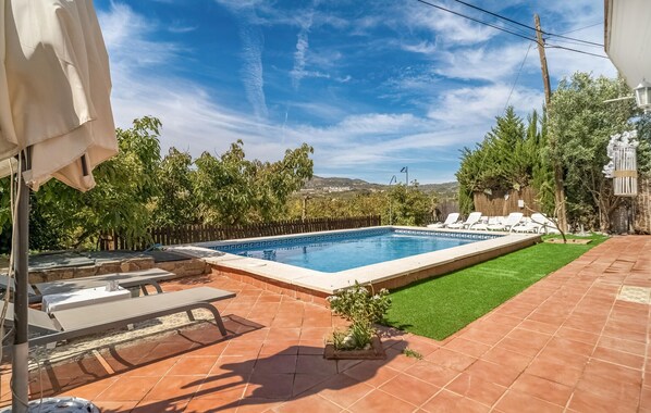 Una piscina rectangular con un borde empedrado, rodeada por una cerca de madera y abundante vegetación.