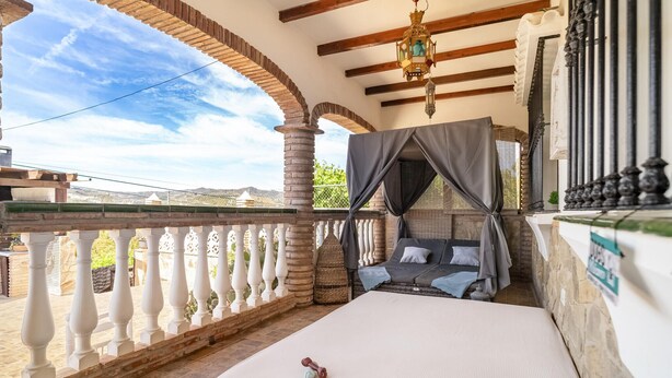 Un balcon avec un lit, une lanterne suspendue et une vue sur le paysage.