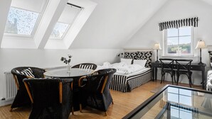 Ein Schlafzimmer mit einem Bett, einem runden Esstisch, Korbstühlen, einem Schreibtisch mit Stuhl und einem Fenster mit Vorhängen.