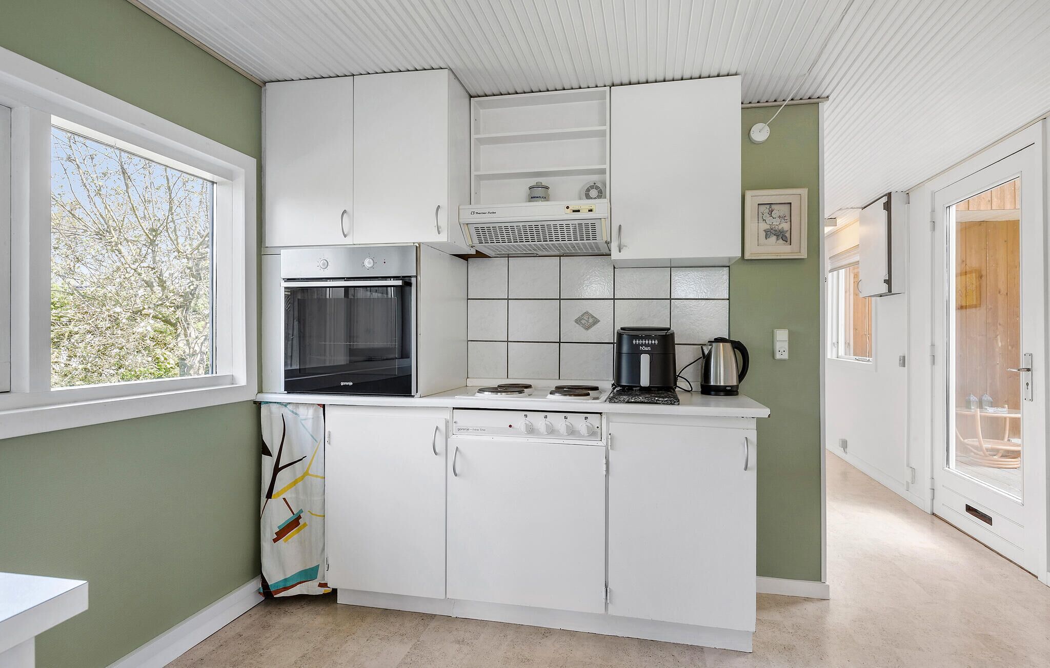 A compact kitchen with a built-in oven, a coffee maker, and a kettle on the countertop.