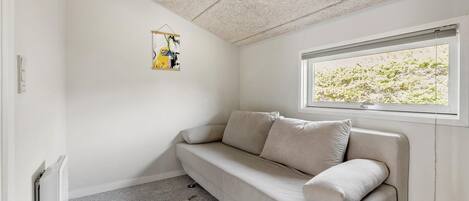 A room with a beige sofa, a hanging abstract painting, a radiator, a window with a view of greenery, and a textured ceiling.