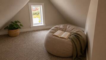 A cozy reading nook with a bean bag chair, a potted plant, and a window with a view of greenery.