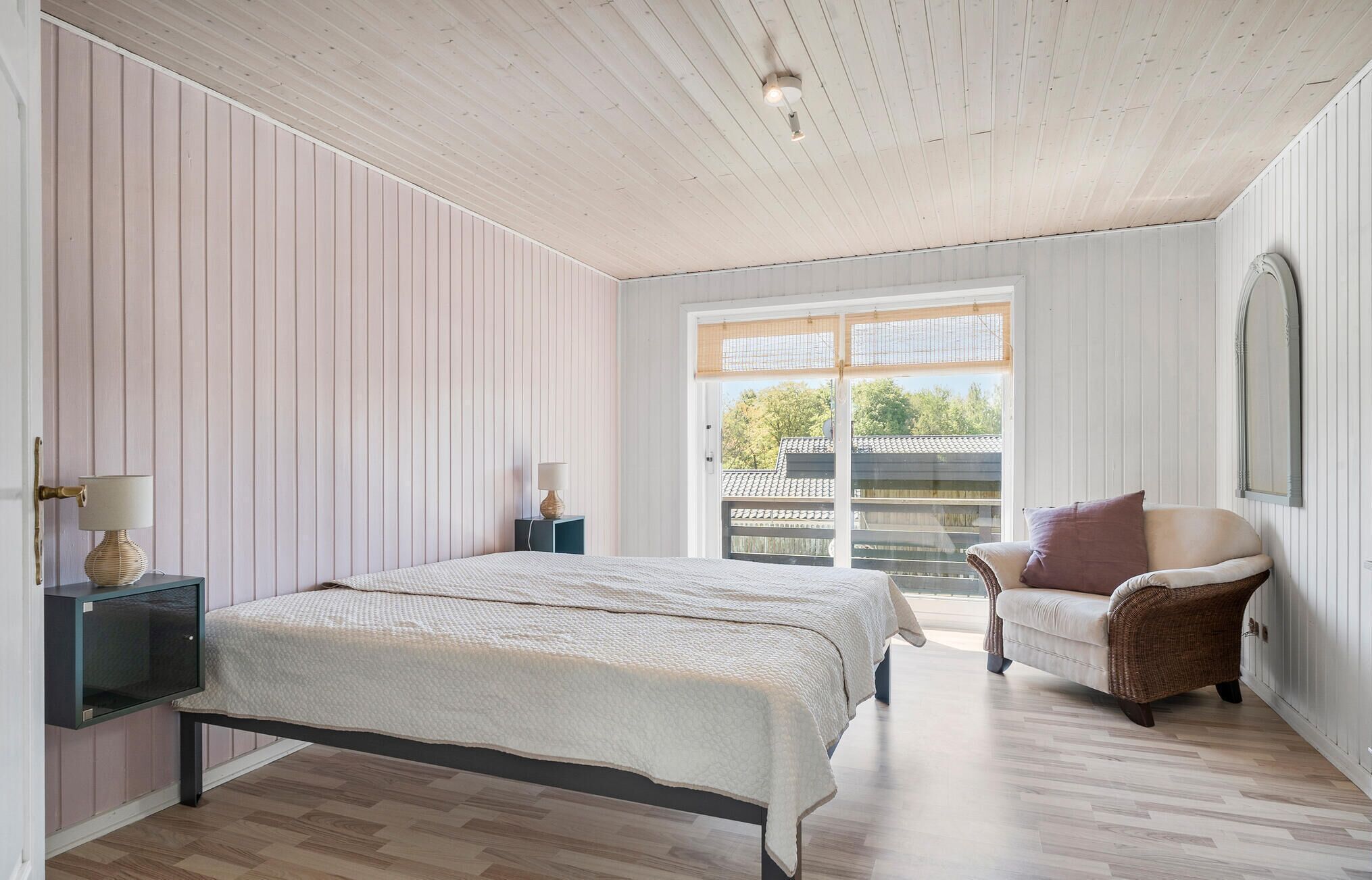 A bedroom with a bed, bedside tables, a chair, and a large window with a view of the outside.