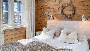 Ett sovrum med en sänggavel i trä, en rund väggdekoration, två sänglampor och en mjukt, fluffigt pläd.