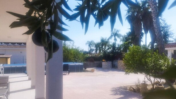 Un patio con un edificio blanco, un árbol pequeño y un muro de piedra.