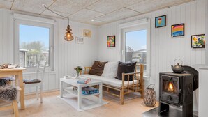A cozy room with a white sofa, a table with board games, a wooden chair, a woven lantern, and a wood-burning stove. - Beautiful home in Otterup with WiFi (Otterup)