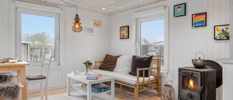 Ein gemütliches Zimmer mit einem weißen Sofa, einem Tisch mit Gesellschaftsspielen, einem Holzstuhl, einer gewobenen Laterne und einem Kaminofen.