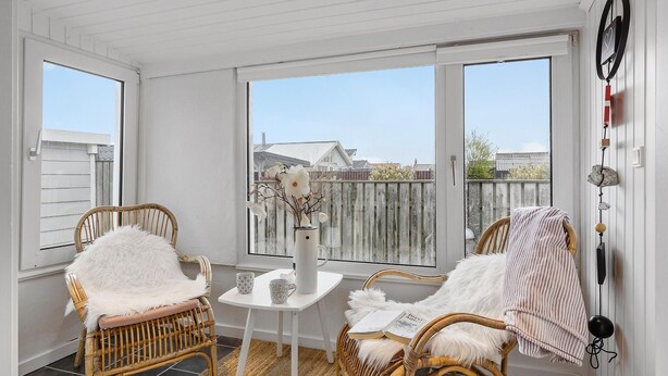 A bright, airy room with wicker chairs, a white table, and a view of a wooden fence and houses through large windows. - Beautiful home in Otterup with WiFi (Otterup)