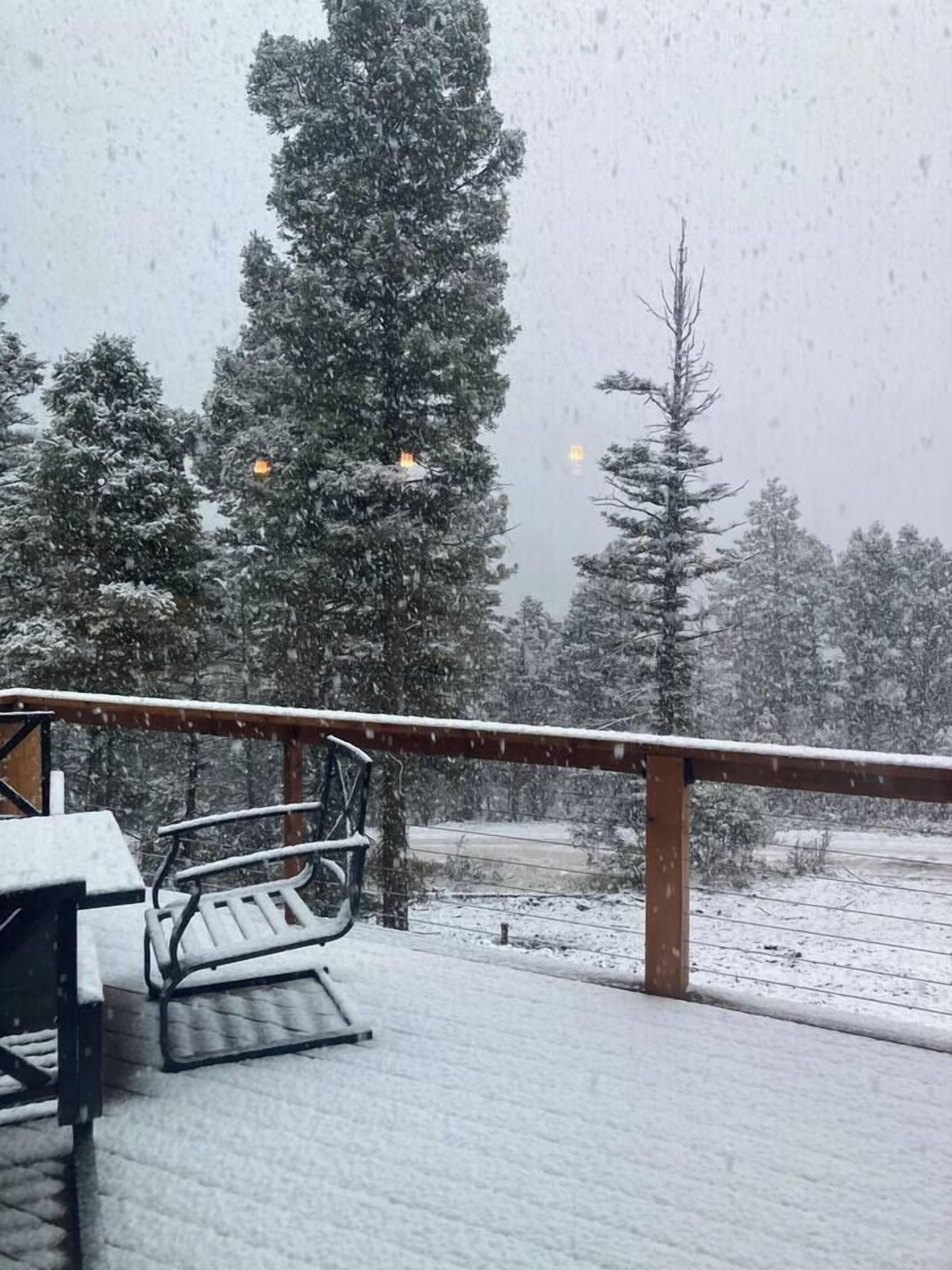 A snow-covered deck with a metal railing and a bench.
