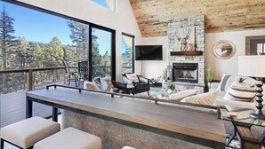 Un salon moderne avec une cheminée en pierre, de grandes fenêtres et un plafond en bois.
