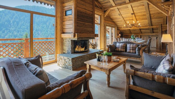 A cozy log cabin interior with a stone fireplace, wooden furniture, and a balcony overlooking a forested mountain. - La Grange au Merle - mountain break for 12 with spa - OVO Network (Châtel)