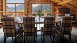 A wooden dining area with a table set for six, large windows with mountain views, and a chandelier. - La Grange au Merle - mountain break for 12 with spa - OVO Network (Châtel)