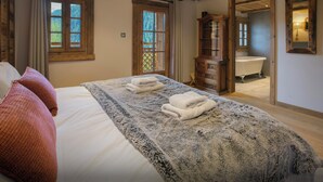 A bedroom with a large bed, wooden ceiling beams, a wooden cabinet, and a bathroom visible through an open door. - La Grange au Merle - mountain break for 12 with spa - OVO Network (Châtel)
