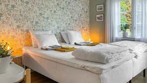 A neatly made bed with white bedding, a small bedside table with a lamp, and a window with a view of greenery. - Awesome home in Västervik with kitchen (Västervik)