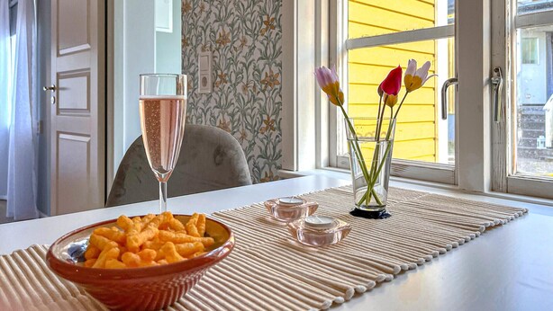 A table with a bowl of snacks, a glass of champagne, and a vase with flowers. - Awesome home in Västervik with kitchen (Västervik)