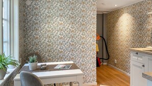 A room with floral wallpaper, a dining table with chairs, a potted plant, and a kitchen area with cabinets and a countertop. - Awesome home in Västervik with kitchen (Västervik)