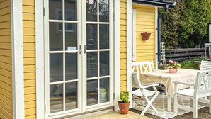 A yellow house with a white door and windows, a small patio with a table and chairs, and a potted plant. - Awesome home in Västervik with kitchen (Västervik)