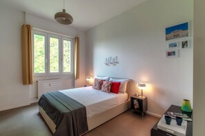 Une chambre à coucher comprenant un lit, des lampes de chevet, un radiateur, une fenêtre avec des rideaux et des œuvres d’art murales.