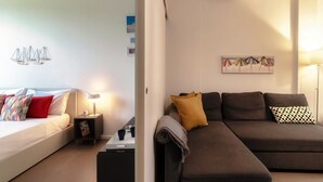 A modern hotel room with a bed, a sofa, a small table with a lamp, and a wall-mounted air conditioner. - Luci A Lago - MyHomeinComo (Como)