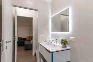 Een moderne badkamer met een witte wastafel, een spiegel en een plant in pot.