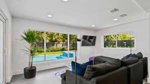 A modern living room with a large window, a black sofa, and a potted plant.