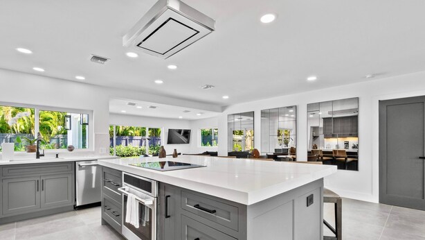 A modern kitchen with a large island, grey cabinetry, and a dishwasher.