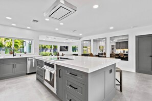 A modern kitchen with a large island, grey cabinetry, and a dishwasher. - Stunning Poolside Luxury Retreat (Fort Lauderdale)