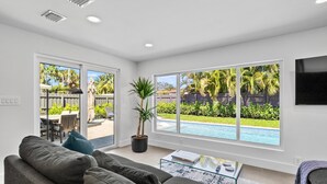 A modern living room with a large window, a sofa, a coffee table, and a potted plant.