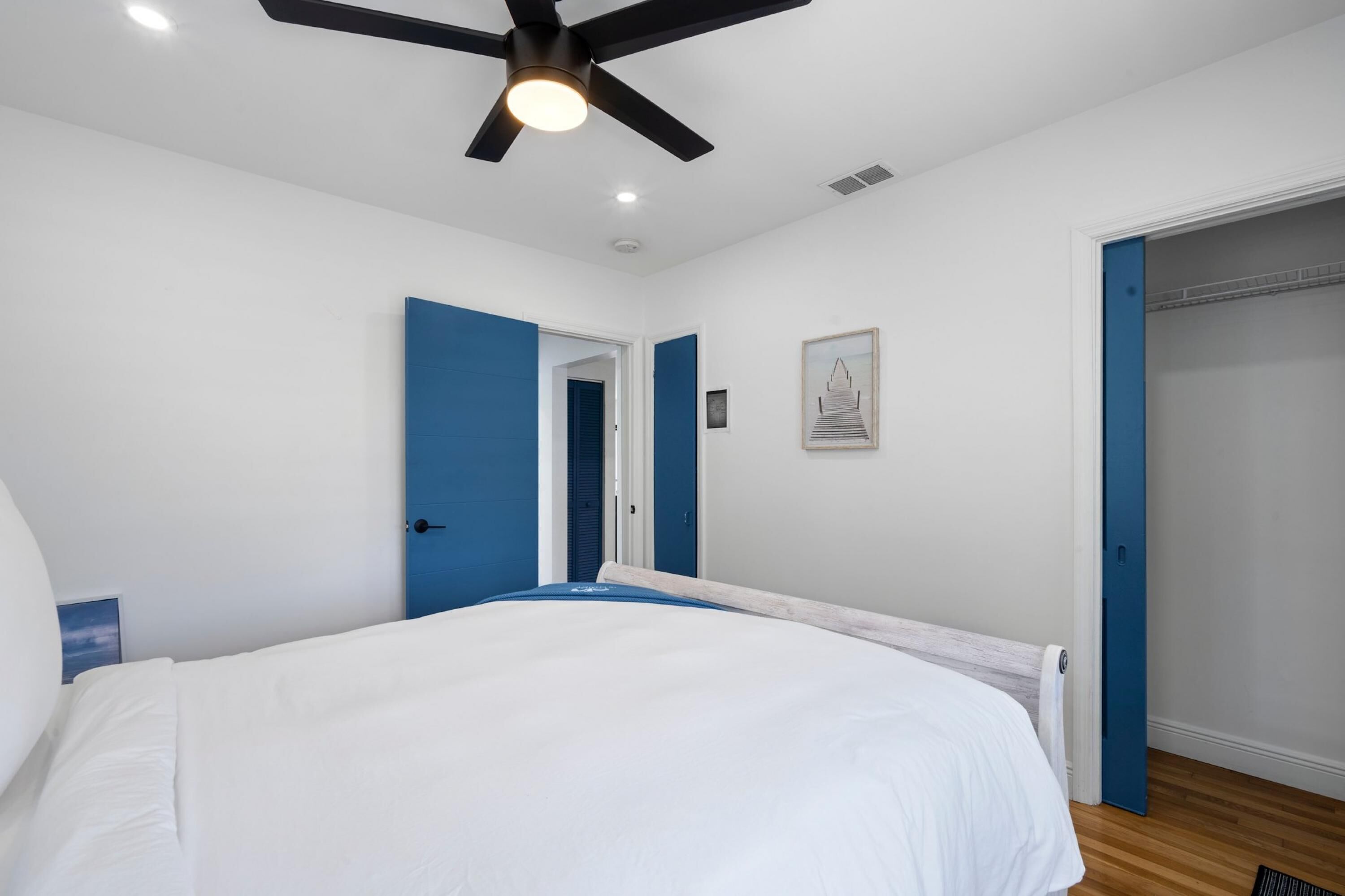 A bedroom with a bed, a ceiling fan, a door leading to a closet, and a framed picture on the wall.